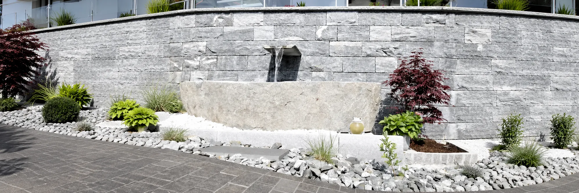 Gestaltete Gartenanlage mit Natursteinmauer, Wandbrunnen und rotem Ahorn als Beispielprojekt im Allgäu