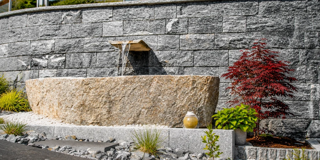 Gartenbrunnen aus Naturstein mit Granittrog und plätscherndem Wasserauslauf